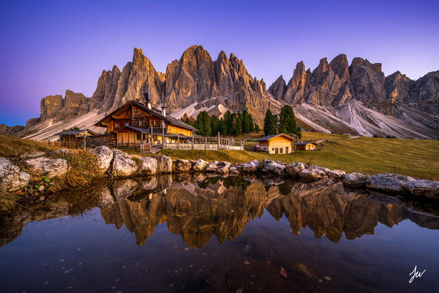 Sunset over Geisler Alm in the Dolomites, Italy, with alpine meadows and dramatic mountain peaks glowing in warm evening light.