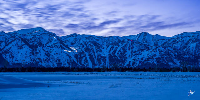 Sunset over Jackson Hole Mountain Resort in Wyoming, with alpenglow lighting the snowy slopes and surrounding Teton peaks.