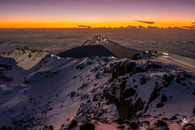 Climbers ascending Mount Kilimanjaro at sunrise with Mawenzi Peak rising in the background.