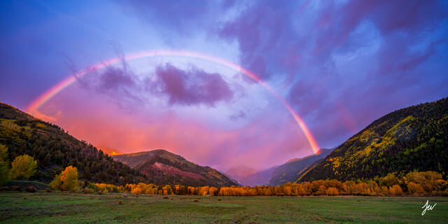 Rainbow over Telluride, Colorado, with golden autumn trees and dramatic storm clouds in the San Juan Mountains.