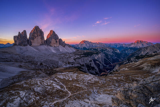 Sunrise over Tre Cime di Lavaredo in the Dolomites, Italy, with golden light illuminating the rugged peaks and alpine landscape.
